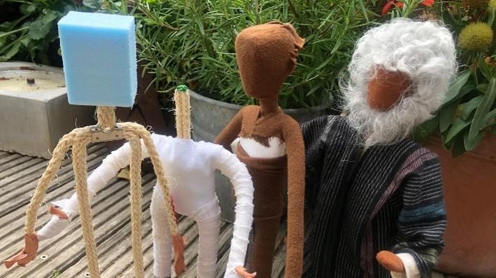 Vier handgefertigte Stofffiguren stehen auf einer Holzterrasse, eine Figur hat weißes Haar und einen weißen Bart.