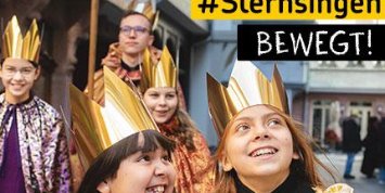 Sternsinger*innen in goldenen und bunten Gewändern mit Kronen ziehen durch eine Straße.