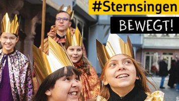 Sternsinger*innen in goldenen und bunten Gewändern mit Kronen ziehen durch eine Straße.