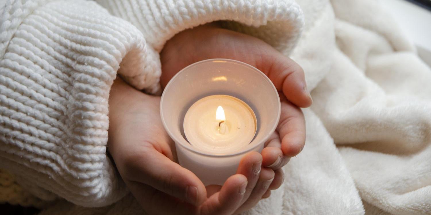 Ein Paar Kinderhände hält behutsam eine kleine brennende Kerze.