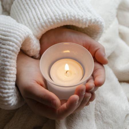 Ein Paar Kinderhände hält behutsam eine kleine brennende Kerze.