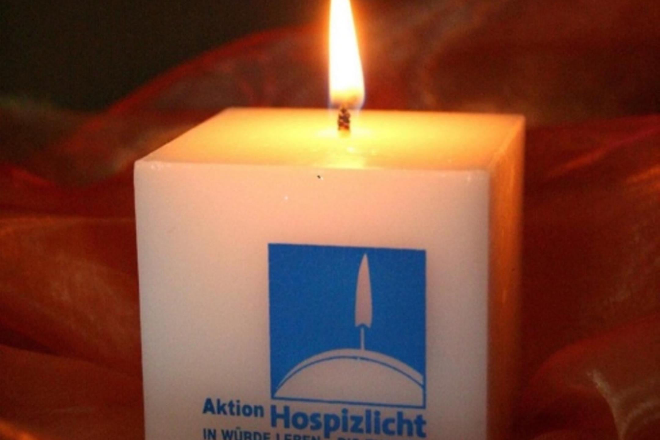 Weiße Hospizkerze mit brennender Flamme auf rotem Stoff.