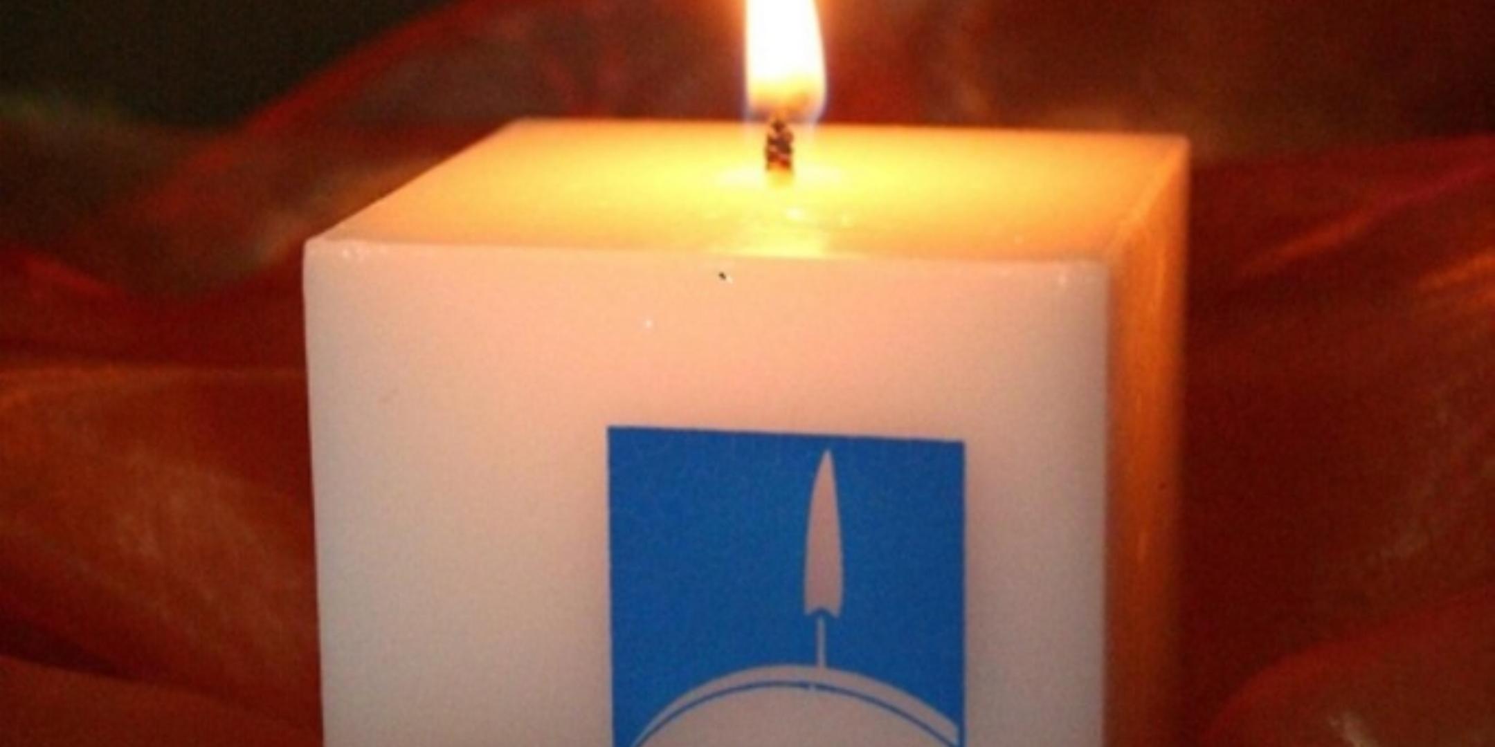 Weiße Hospizkerze mit brennender Flamme auf rotem Stoff.