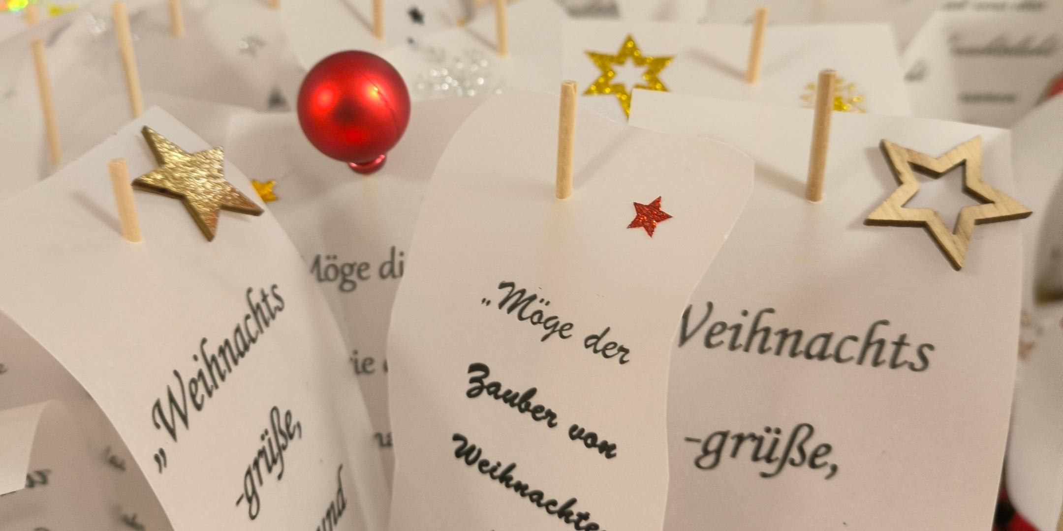 Mehrere kleine Kärtchen mit Weihnachtsgrüßen, verziert mit bunten Sternen und Kugeln, stehen dicht aneinander wie ein festlicher Grußgarten