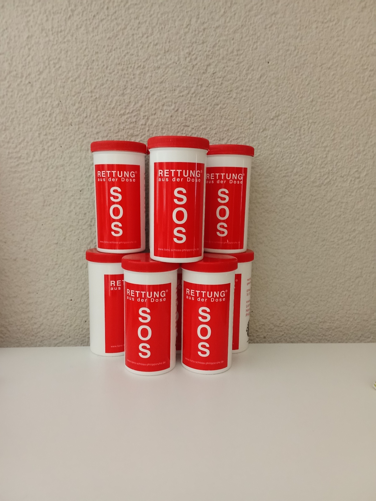 Mehrere rote „SOS – Rettung aus der Dose“-Behälter sind zu einer kleinen Pyramide aufgestellt.