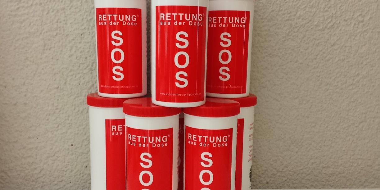 Mehrere rote „SOS – Rettung aus der Dose“-Behälter sind zu einer kleinen Pyramide aufgestellt.