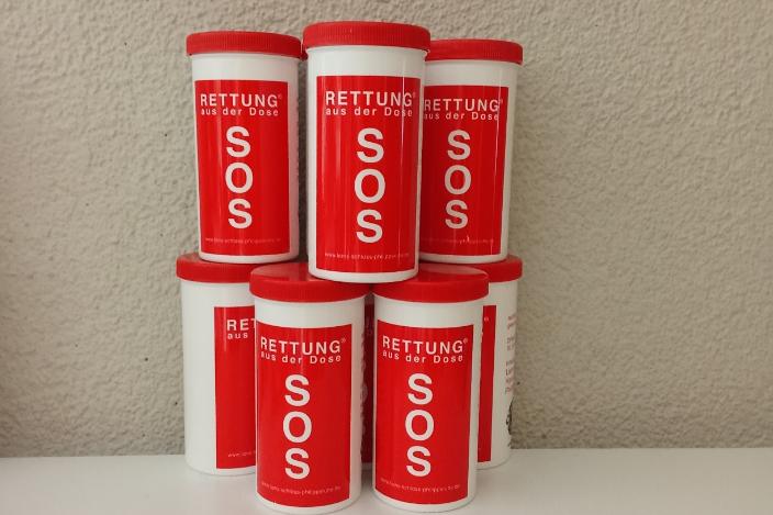 Mehrere rote „SOS – Rettung aus der Dose“-Behälter sind zu einer kleinen Pyramide aufgestellt.