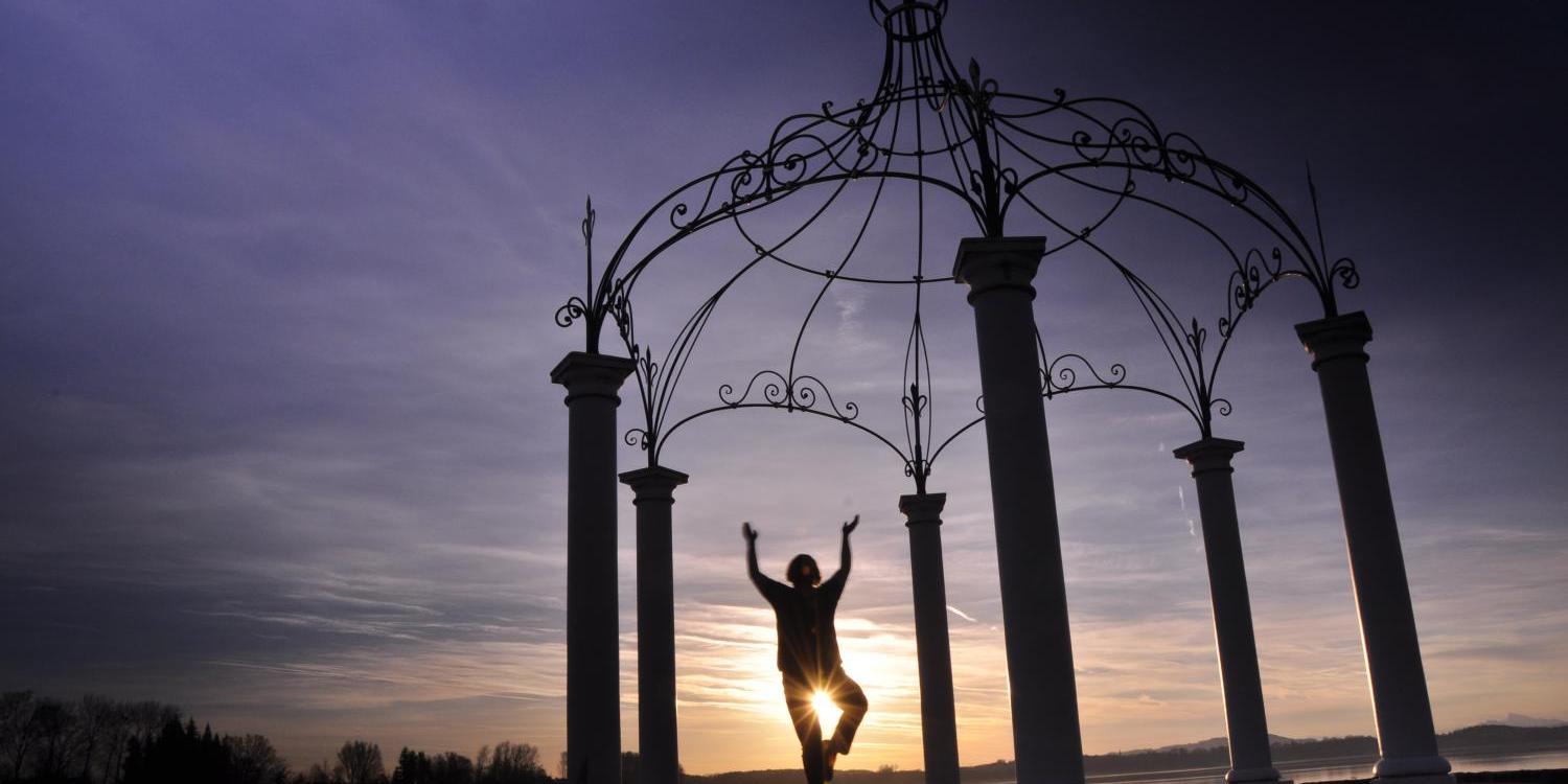 Eine Person steht in einer filigranen Pavillonkonstruktion und posiert im Gegenlicht der untergehenden Sonne.