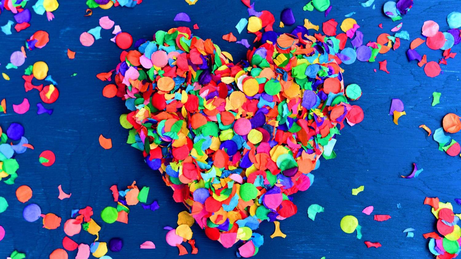 Ein Herz aus buntem Konfetti liegt auf blauem Hintergrund.