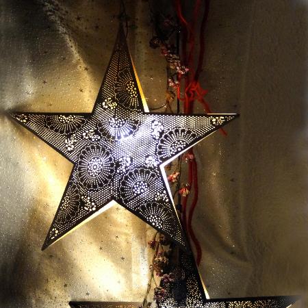 Zwei große, dunkle Metallsterne mit feinen Lochmustern leuchten warm von innen vor einem goldenen Hintergrund.