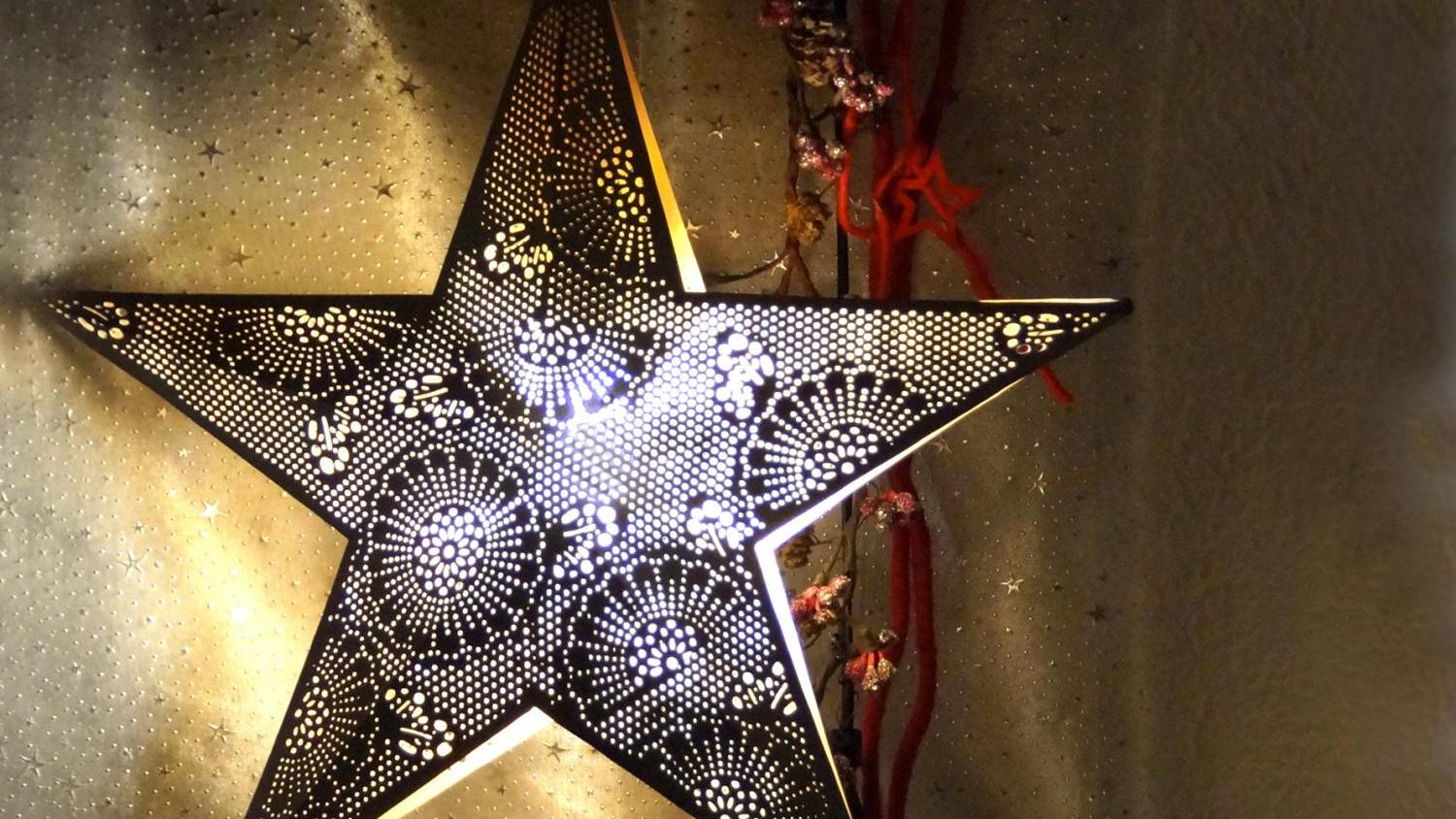 Zwei große, dunkle Metallsterne mit feinen Lochmustern leuchten warm von innen vor einem goldenen Hintergrund.