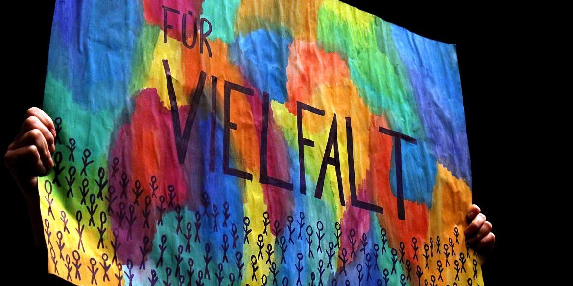 Ein bunt bemaltes Plakat zeigt das Wort „Vielfalt“ über vielen kleinen stilisierten Figuren.