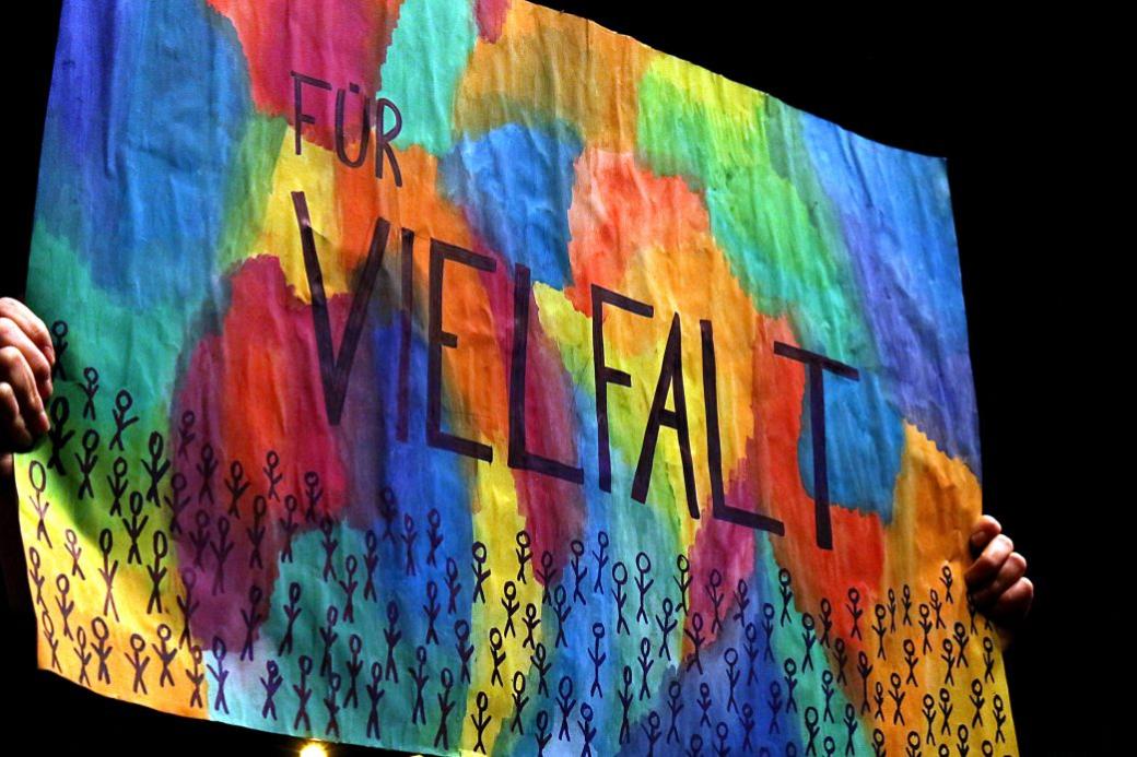 Ein bunt bemaltes Plakat zeigt das Wort „Vielfalt“ über vielen kleinen stilisierten Figuren.