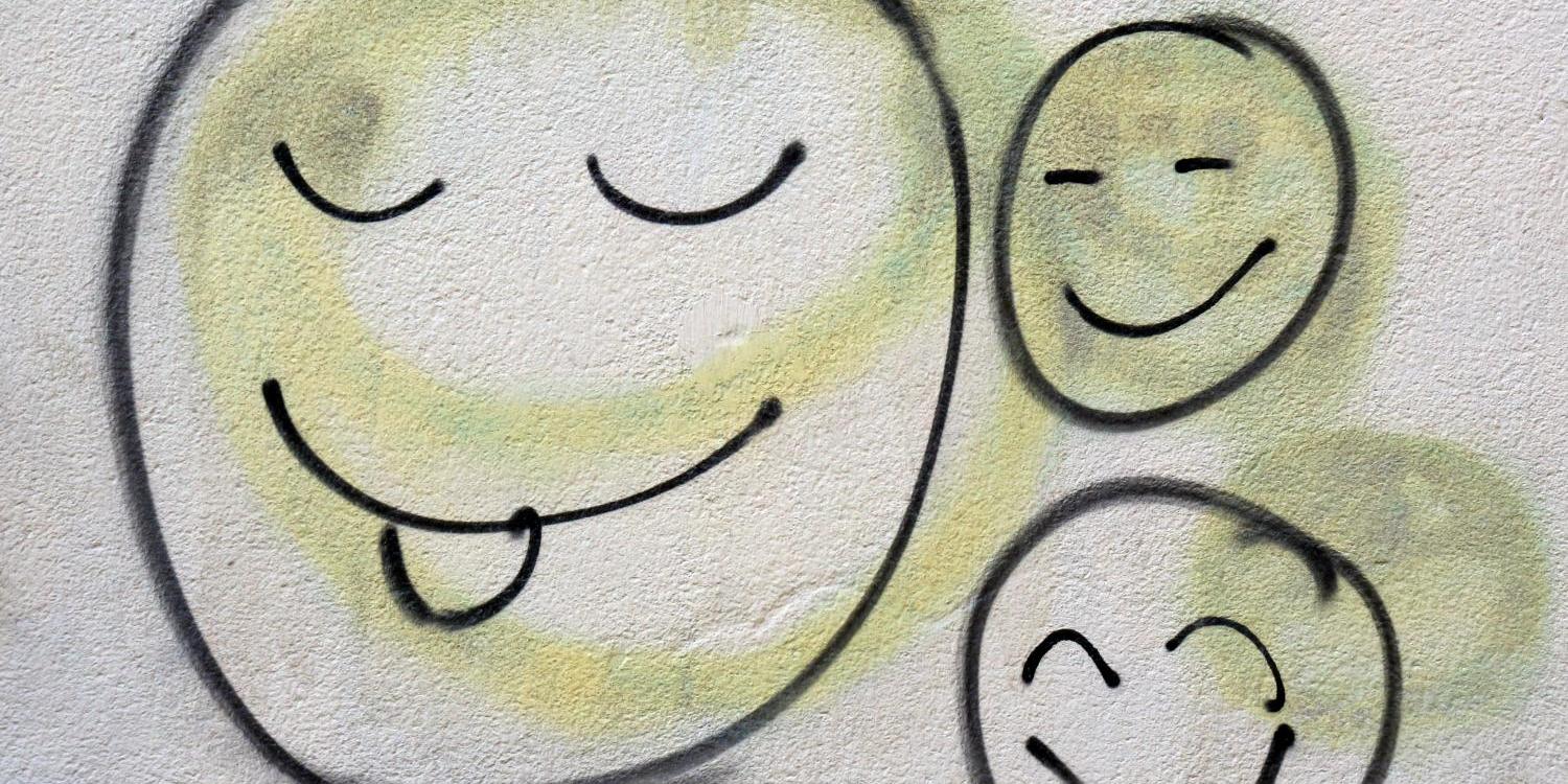 Drei lachende Smileys als Graffiti auf einer hellen Wand.
