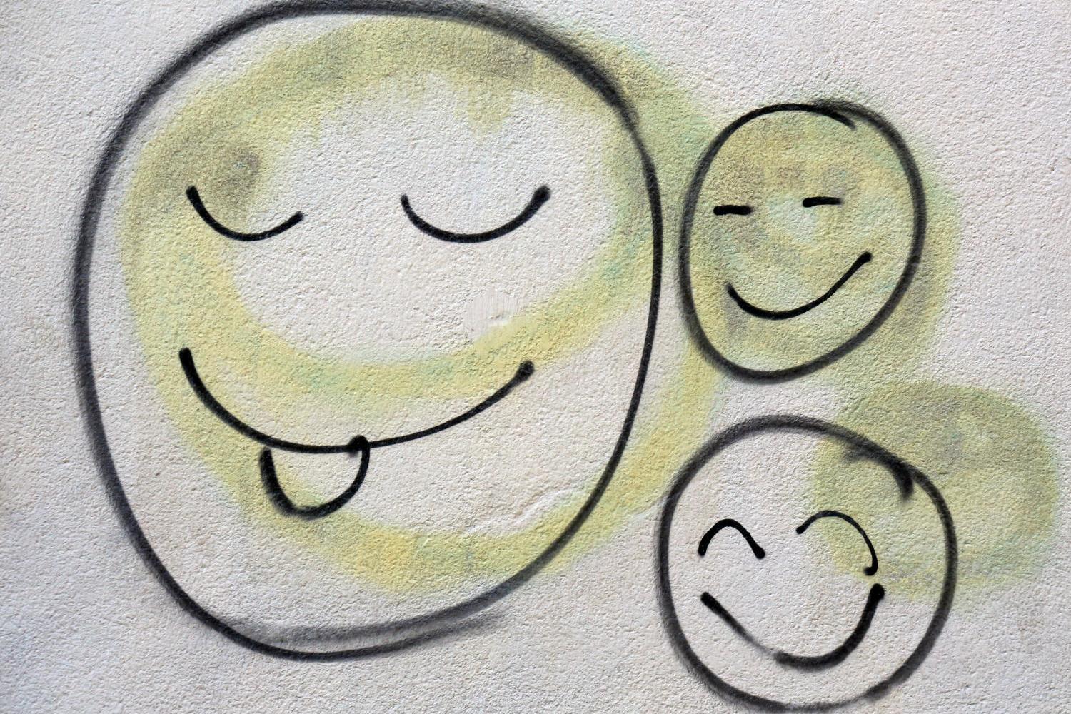Drei lachende Smileys als Graffiti auf einer hellen Wand.