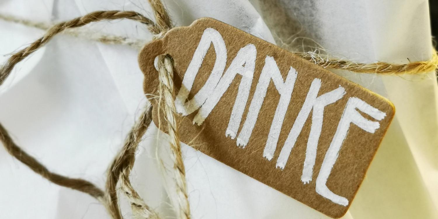 Ein kleines Pappschild mit der handgeschriebenen Aufschrift „DANKE“ ist mit einer Schnur an weißem Verpackungspapier befestigt