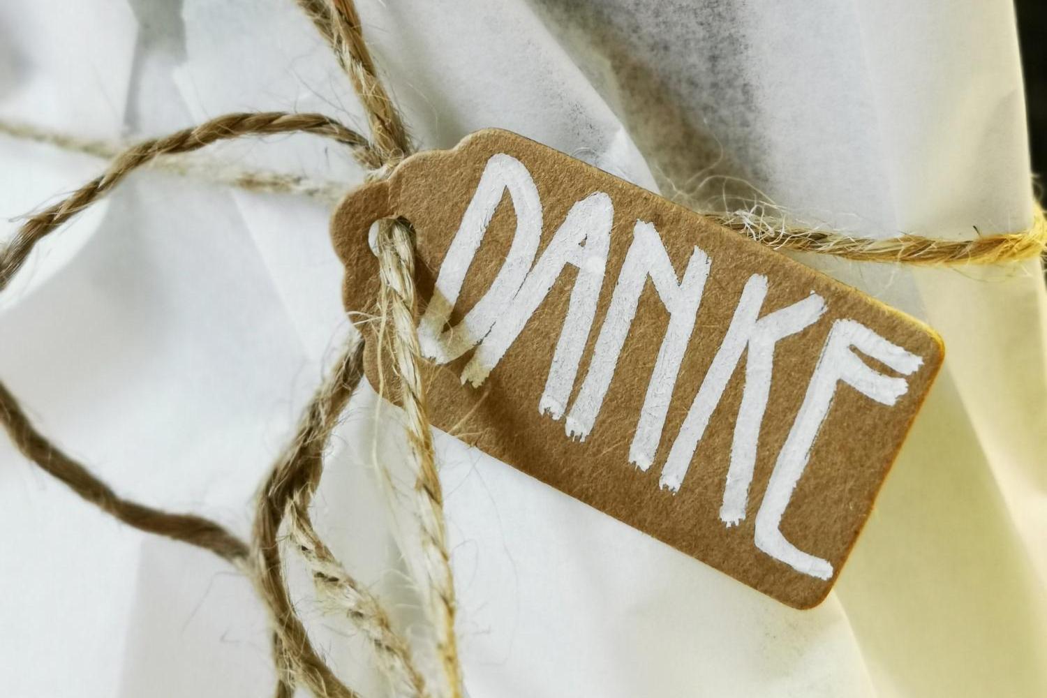 Ein kleines Pappschild mit der handgeschriebenen Aufschrift „DANKE“ ist mit einer Schnur an weißem Verpackungspapier befestigt