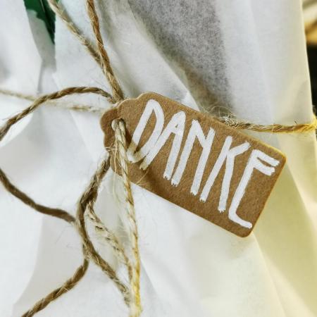 Ein kleines Pappschild mit der handgeschriebenen Aufschrift „DANKE“ ist mit einer Schnur an weißem Verpackungspapier befestigt