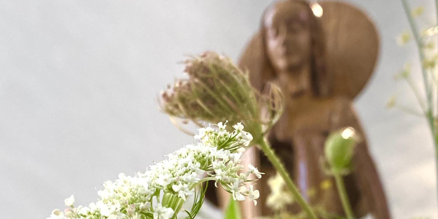 Blumen im Vordergrund, verschwommene Marienstatue im Hintergrund.