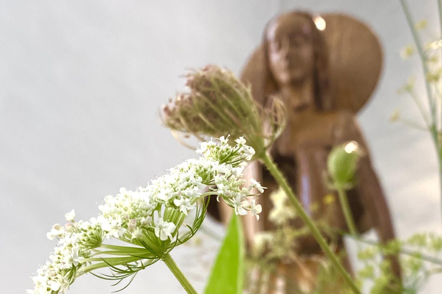 Blumen im Vordergrund, verschwommene Marienstatue im Hintergrund.