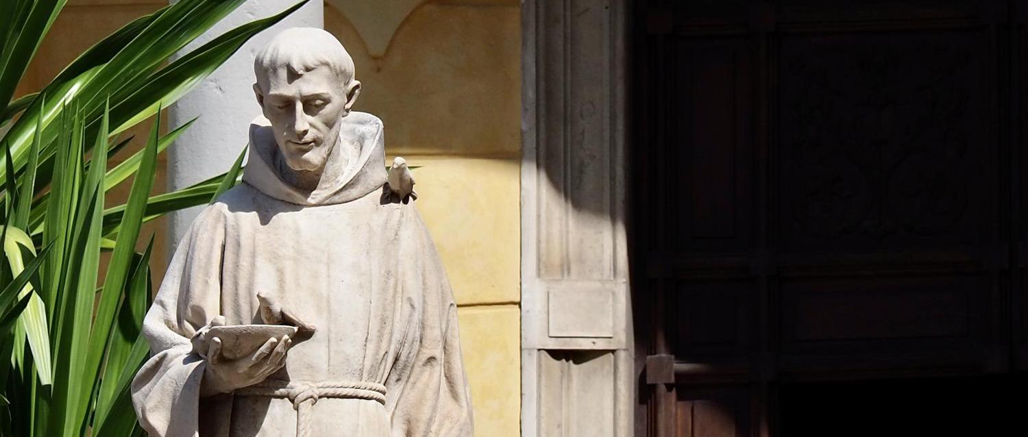Steinstatue eines Mönchs mit Buch in sonnigem Hof neben einer Pflanze