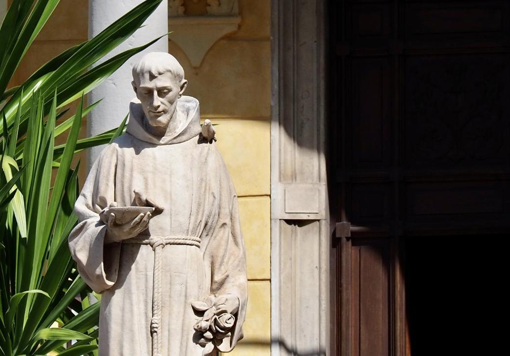 Steinstatue eines Mönchs mit Buch in sonnigem Hof neben einer Pflanze