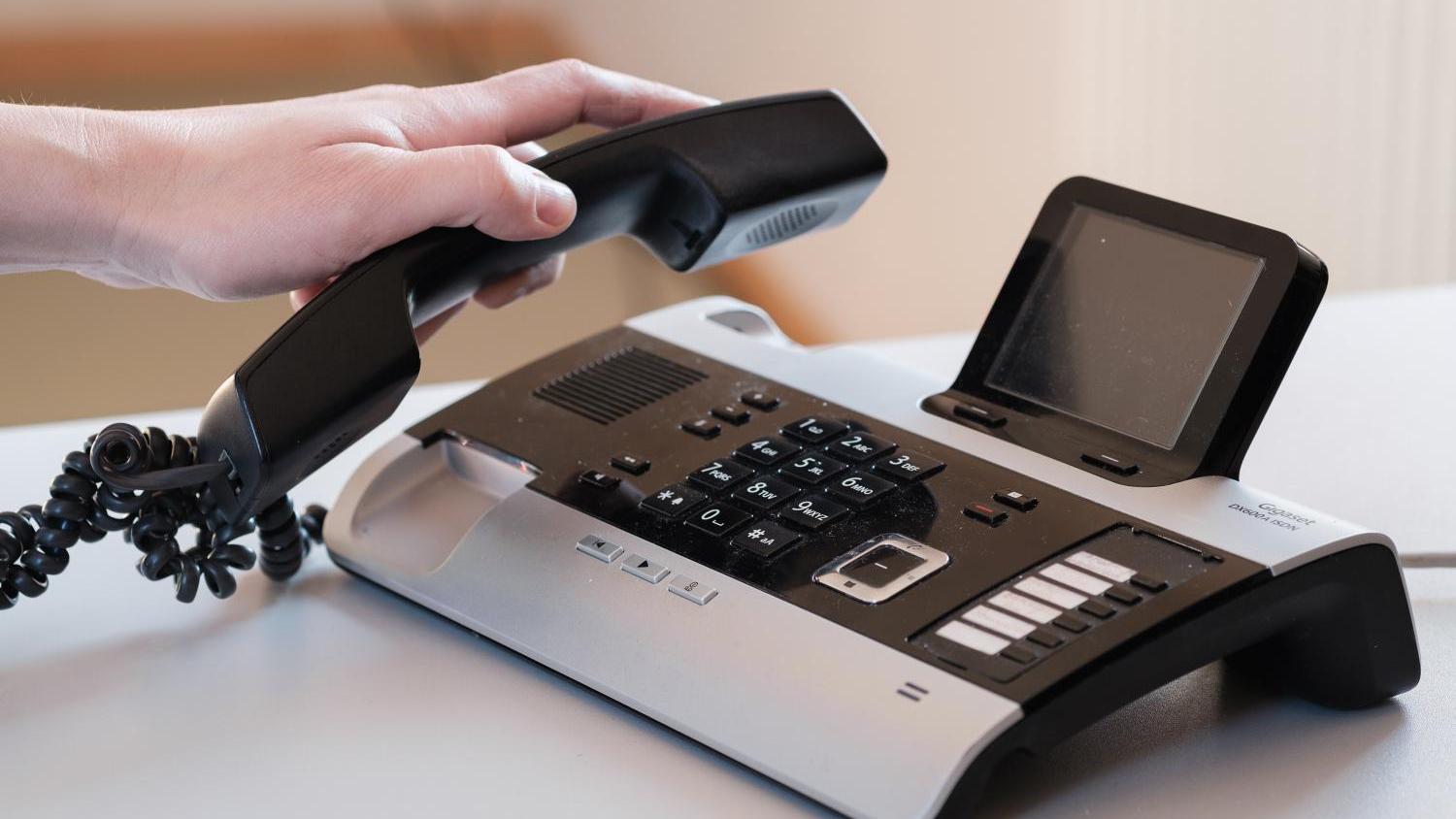 Hand hebt Hörer von modernem Tischtelefon mit Display ab.