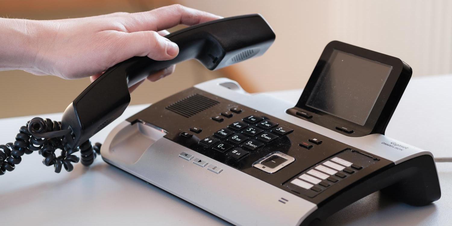 Hand hebt Hörer von modernem Tischtelefon mit Display ab.