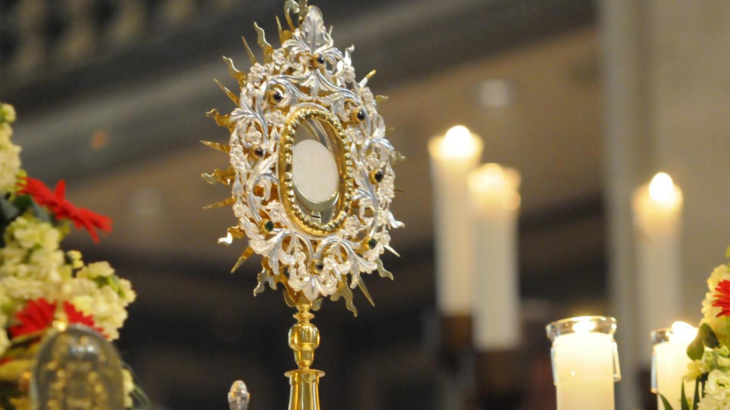 Goldene Monstranz auf einem Altar, umgeben von Kerzen und Blumen.