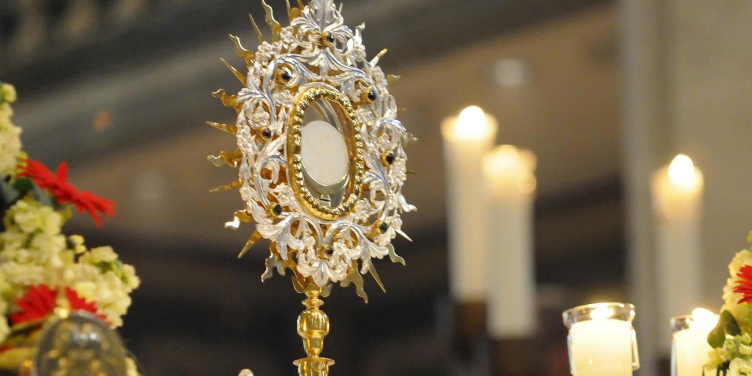 Goldene Monstranz auf einem Altar, umgeben von Kerzen und Blumen.