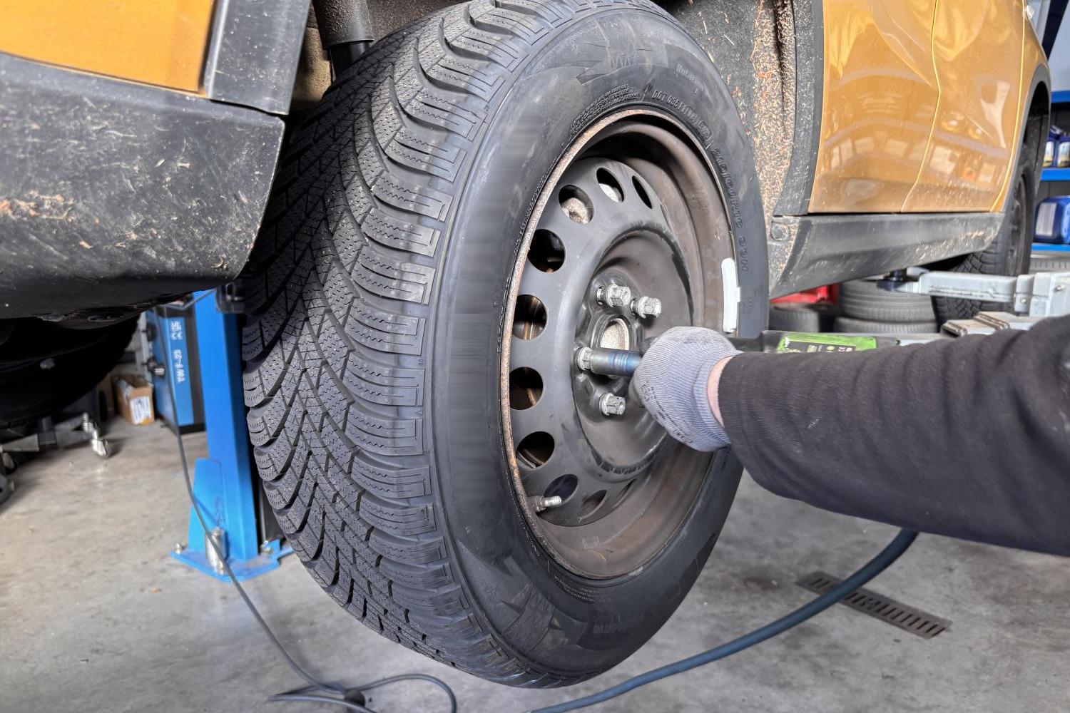 Eine Person zieht an einem hochgebockten Auto das Rad fachgerecht fest.