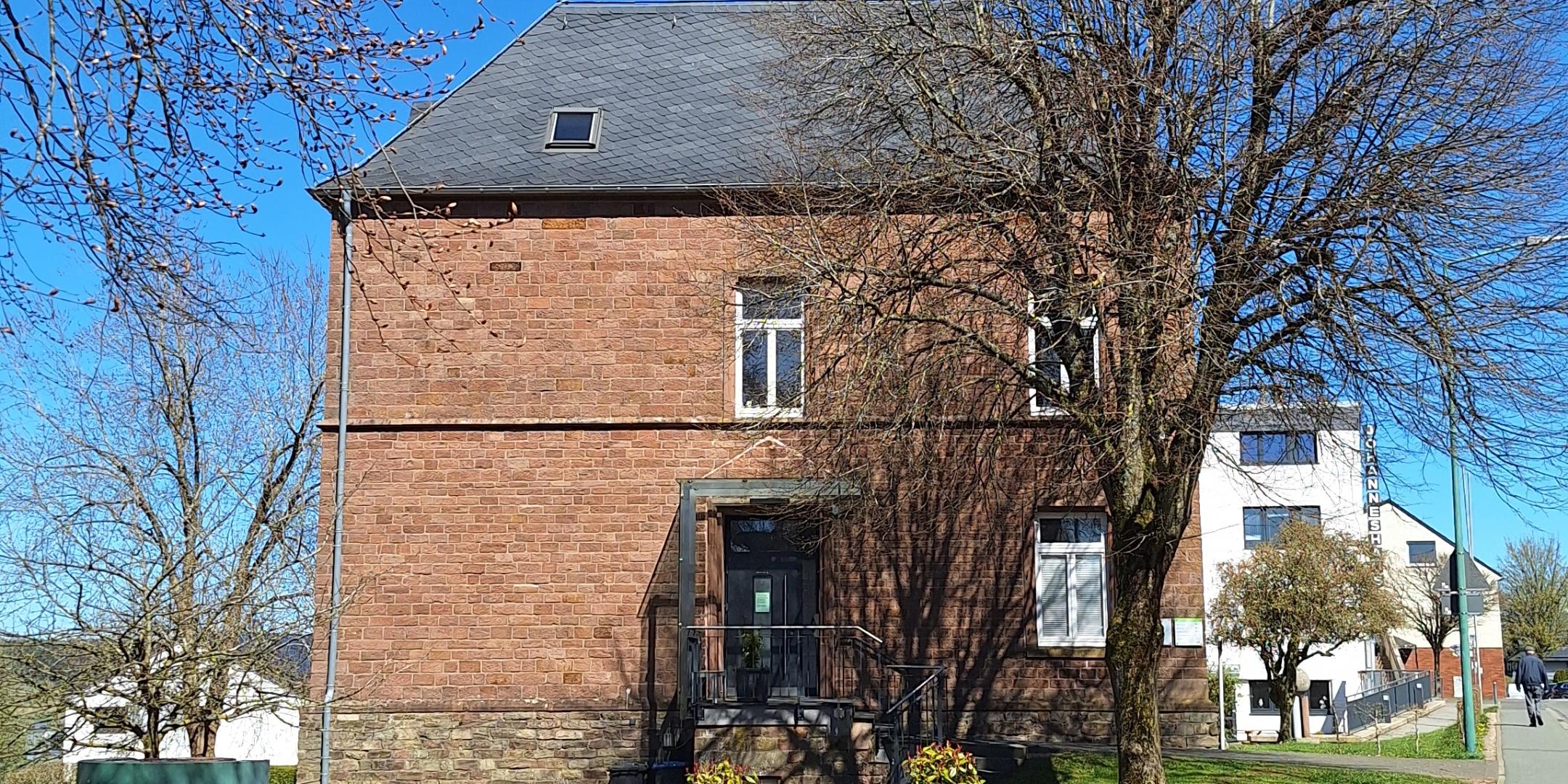 Ein Backsteingebäude an einer ruhigen Dorfstraße, umgeben von Bäumen und Grünflächen