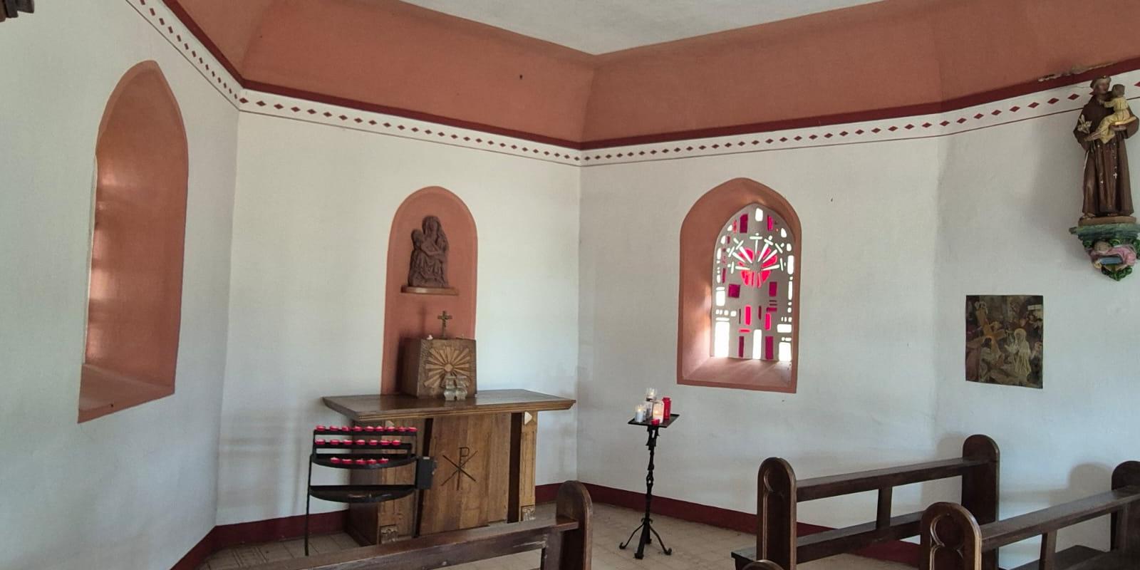 Der Innenraum der St.-Anna-Kapelle mit Holzbänken, einem schlichten Altar, einer Pietà in einer Wandnische und einem farbigen Fenster.