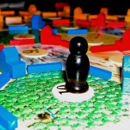 Das Foto zeigt ein Spielbrett mit sechseckigen Feldern, bunten Holzspielsteinen und einer schwarzen Spielfigur auf einem grünen Feld mit der Zahl 10.