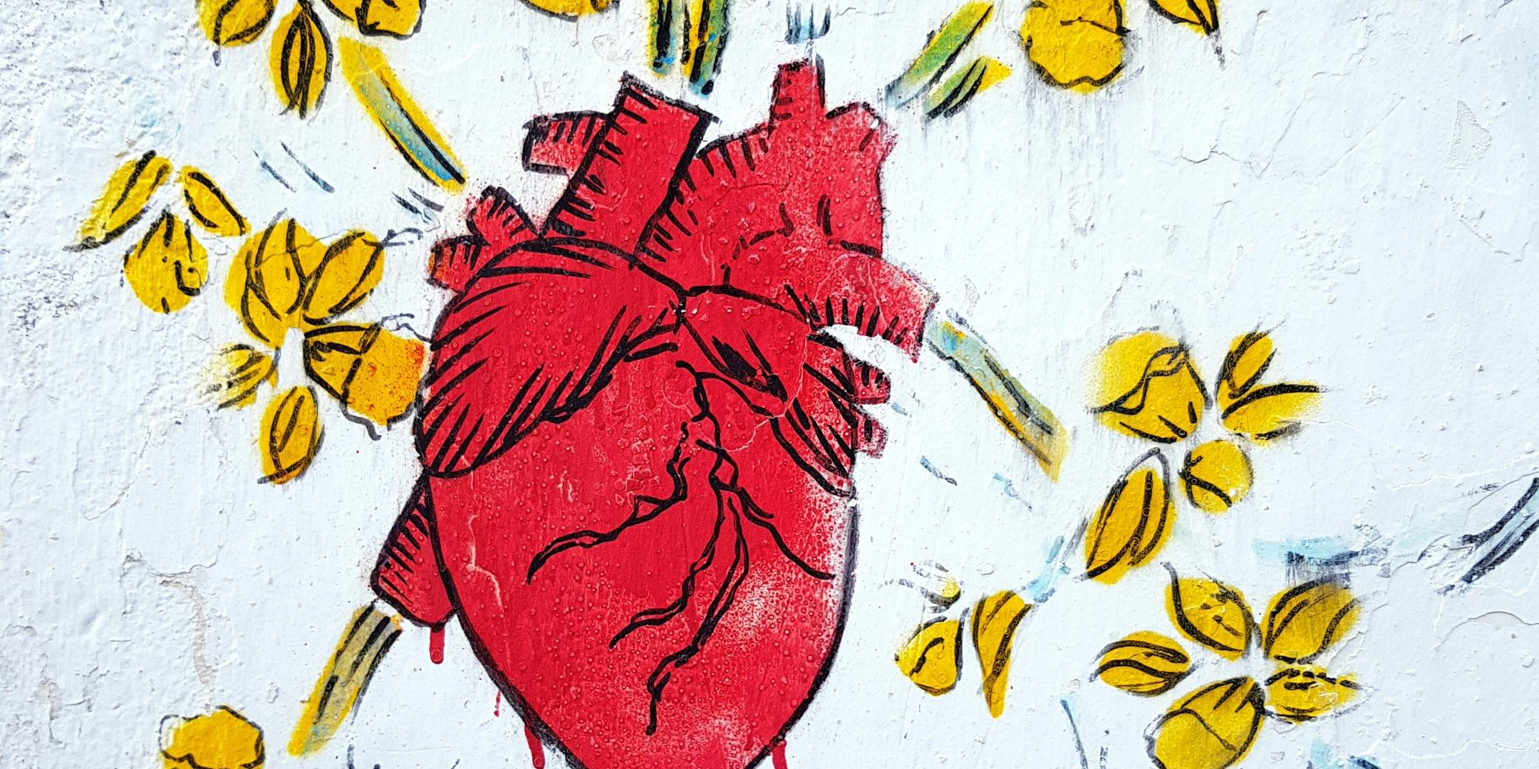 Das Bild zeigt ein rotes anatomisches Herz, umgeben von gelben Blumen, mit handschriftlichem Text darunter, der teilweise lesbar ist.