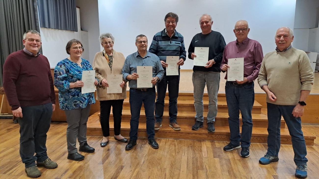 Eine Gruppe von Personen steht gemeinsam in einem Saal und hält Urkunden für eine Ehrung in den Händen.
