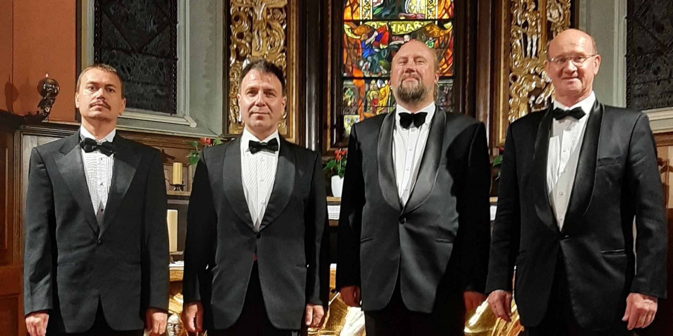 Die vier St. Petersburger Solisten sind ein Ensemble, das in eleganter Kleidung vor einem kunstvollen Altar mit farbigem Glasfenster steht.