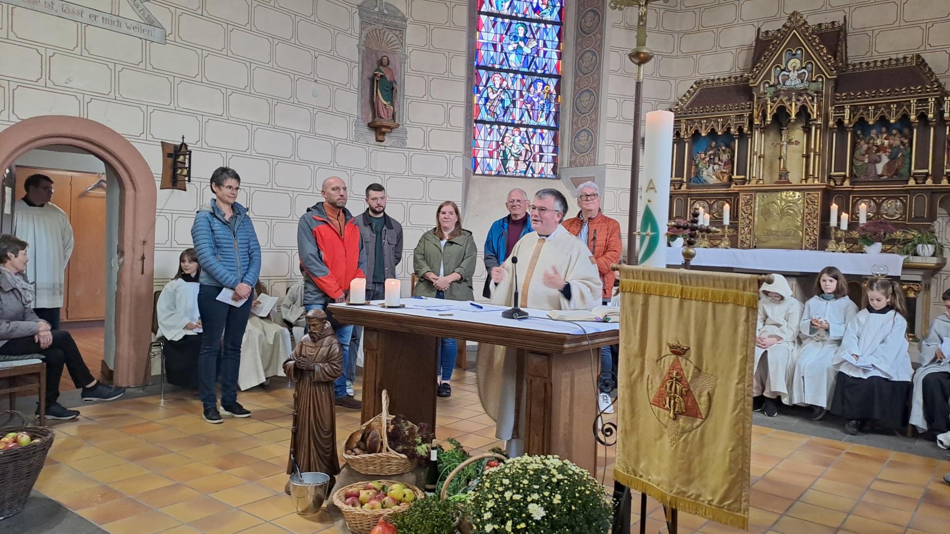 Das Bild zeigt eine feierliche Zeremonie in der Kirche, bei der mehrere Personen um den Altar versammelt sind und ein Geistlicher eine Ansprache hält.