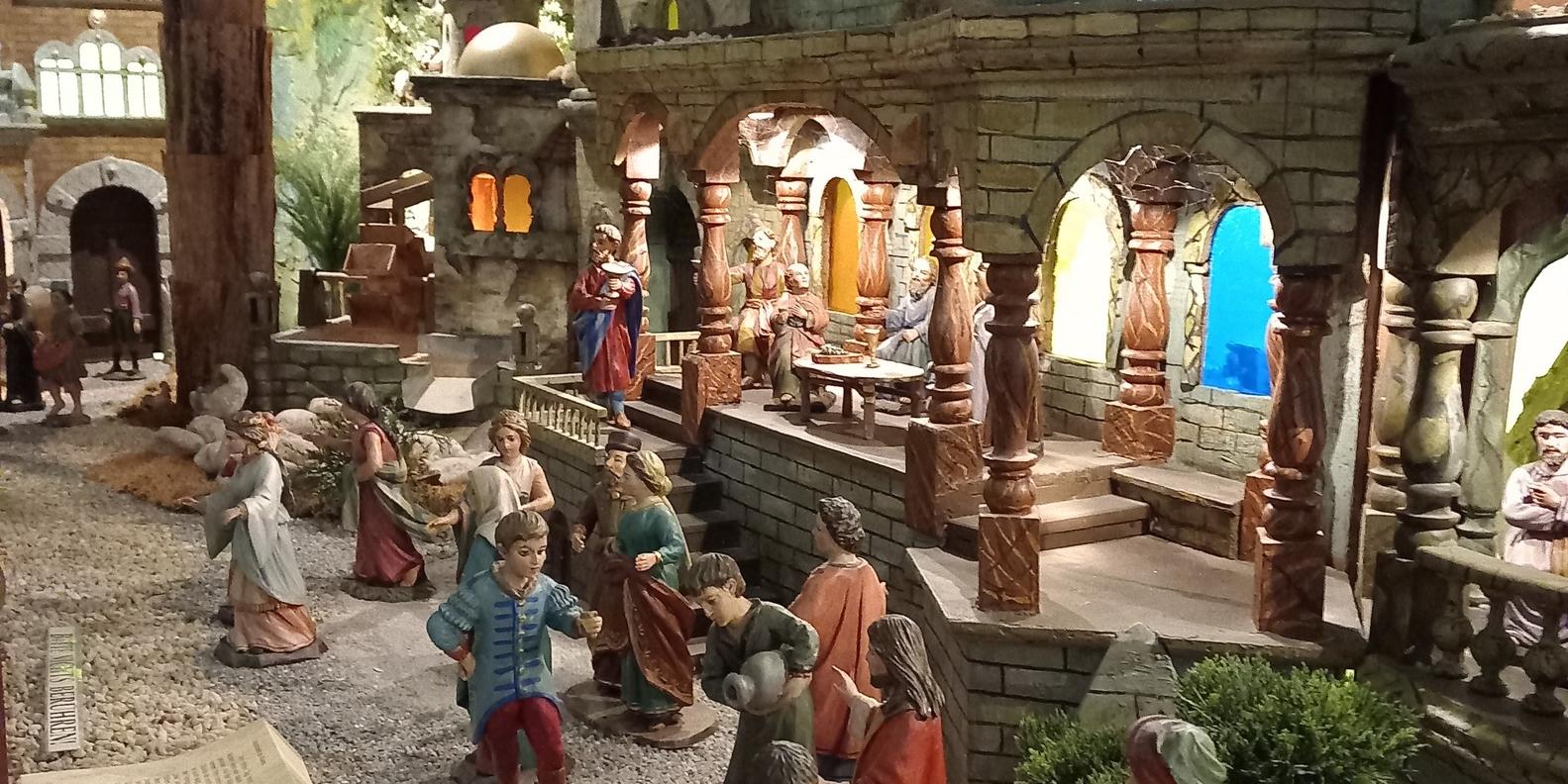 Die Szene zeigt eine detailreiche Weihnachtskrippe mit vielen handgeschnitzten Figuren, die auf einem steinigen Weg vor einem großen orientalisch anmutenden Gebäude stehen, während im Hintergrund weitere Figuren in beleuchteten Arkaden und Häusern das Leben zur Zeit Jesu darstellen. (c) Pfarrer Kai Georg Quirin Die Szene zeigt eine detailreiche Weihnachtskrippe mit vielen handgeschnitzten Figuren, die auf einem steinigen Weg vor einem großen orientalisch anmutenden Gebäude stehen, während im Hintergrund weitere Figuren in beleuchteten Arkaden und Häusern das Leben zur Zeit Jesu darstellen.